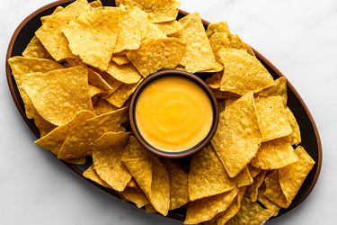 Nacho cheese sauce in a small bowl in the center of a platter, surrounded by tortilla chips.