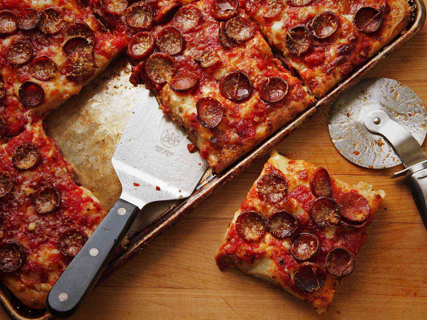 一块方形的意大利辣香肠披萨放在带边的烤盘上，旁边是一整块披萨