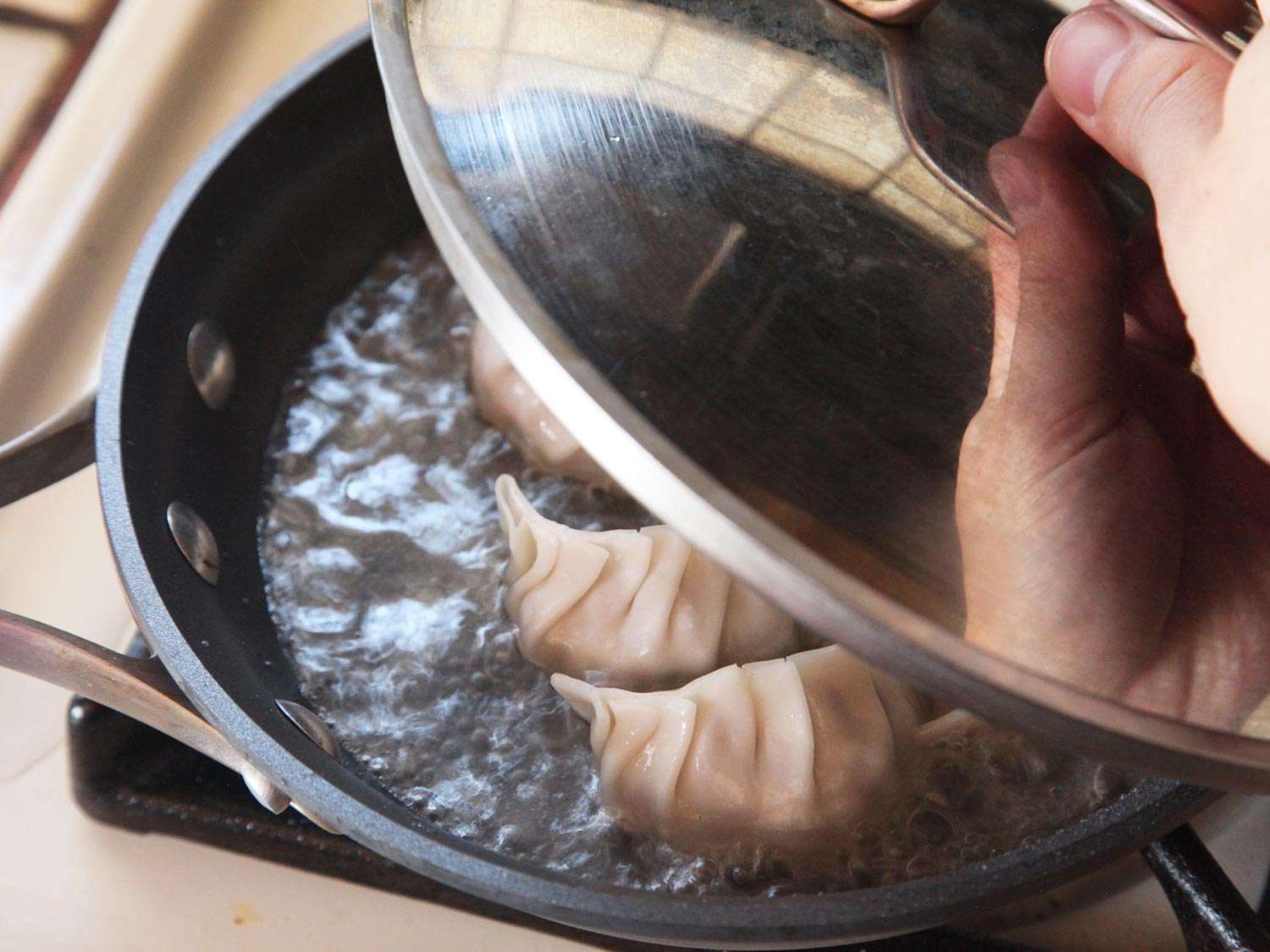 把锅盖盖在装有日式饺子和水的不粘锅上，让饺子蒸熟。
