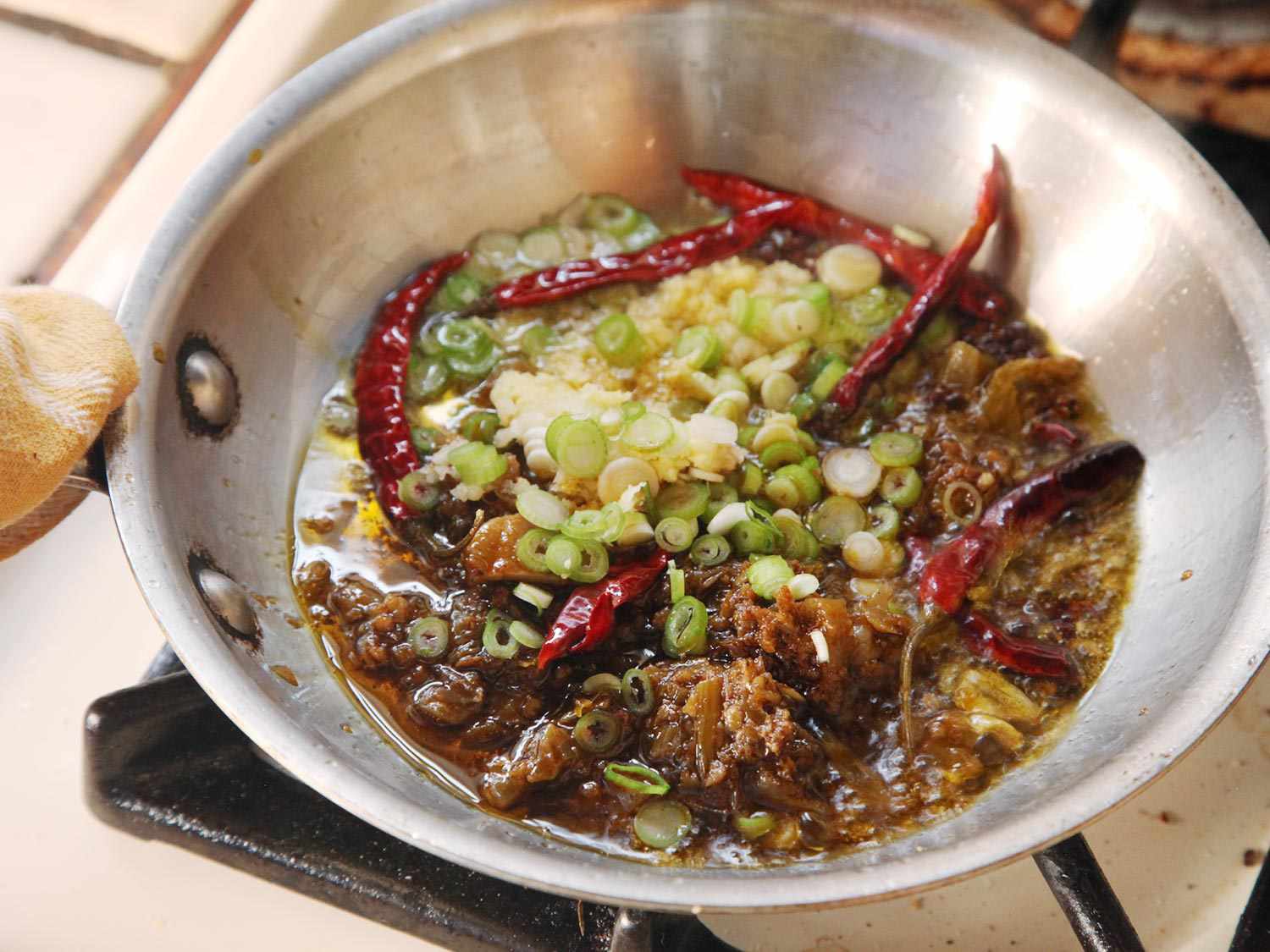 将辣椒、花椒、姜、大蒜和葱花放入小煎锅中轻轻煎炸。