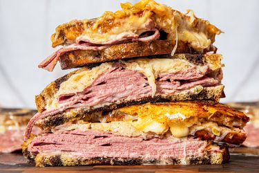 Three reuben sandwich halves stacked on top of each other on a cutting board