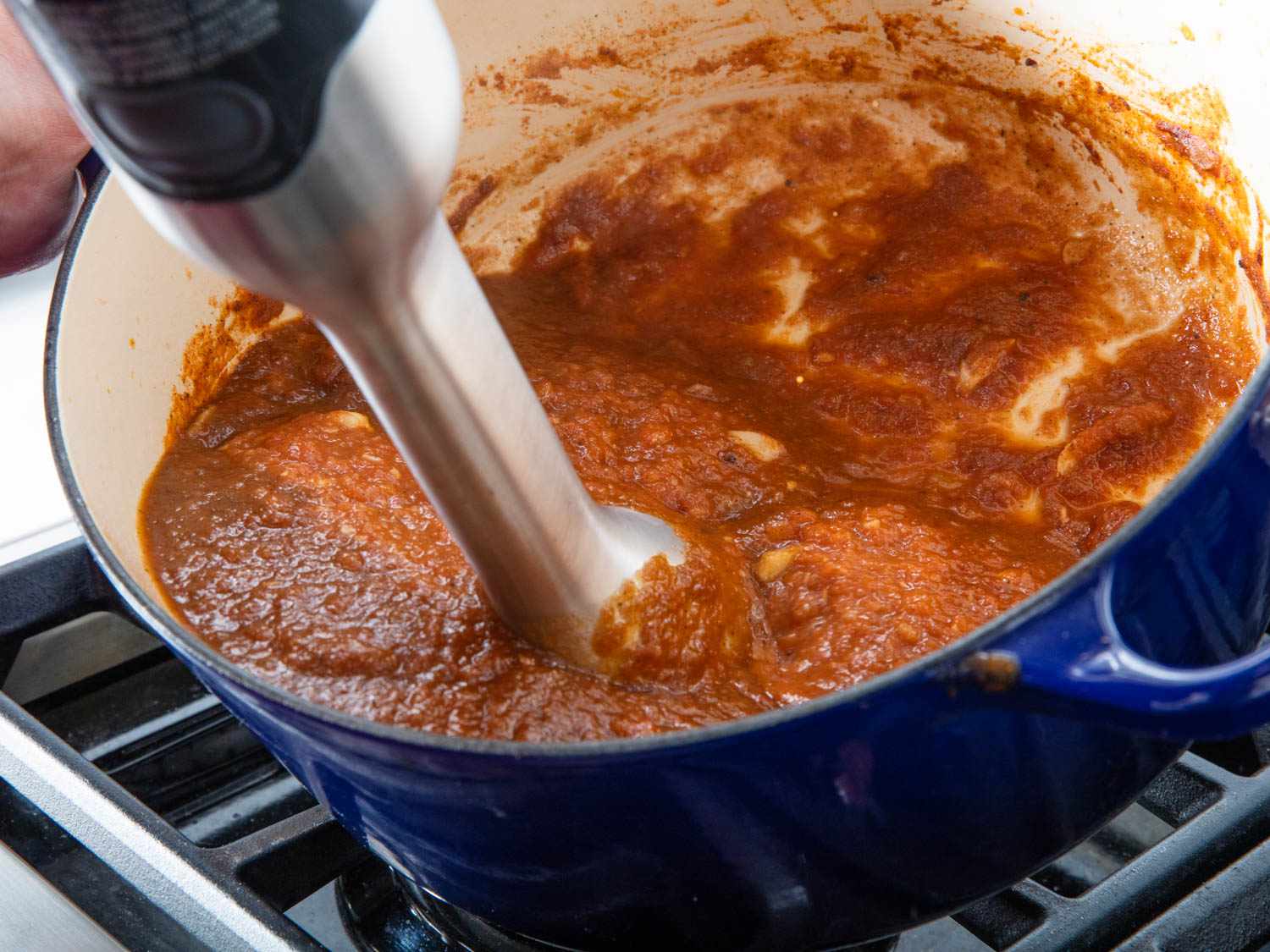 用浸入式搅拌机在搪瓷铸铁荷兰烤箱中搅拌黄油鸡的酱汁。