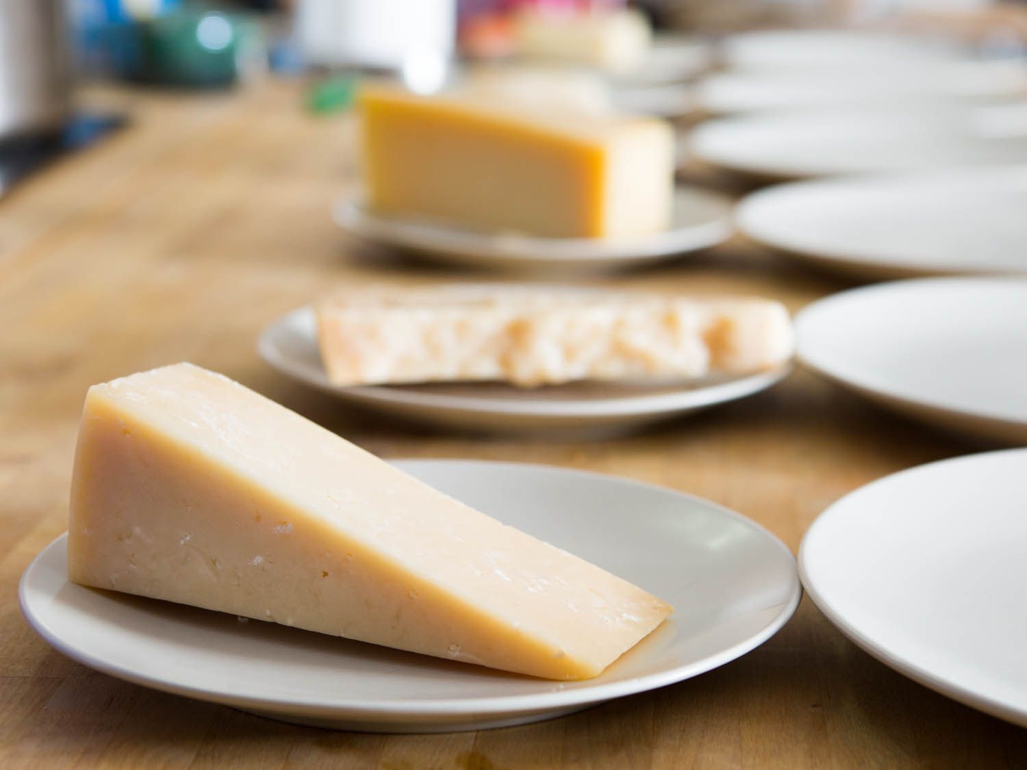 一张桌子，上面摆着十个小白盘子。其中五个盘子上有大块或楔形的奶酪。