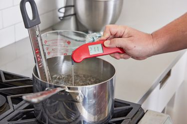 一只手使用一个即时可见的温度计the temperature of water boiling in a saucepan