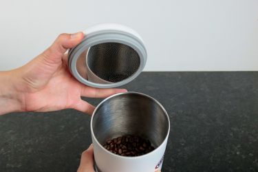 One hand holding the lid of a coffee container and the other holding the body of the container