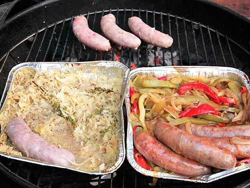 烤架上放着两个铝托盘的香肠(一个放着酸菜和芥末，一个放着辣椒和洋葱)