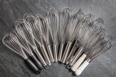 12 ballon whisks laid out in a semi circle on a piece of grey slate