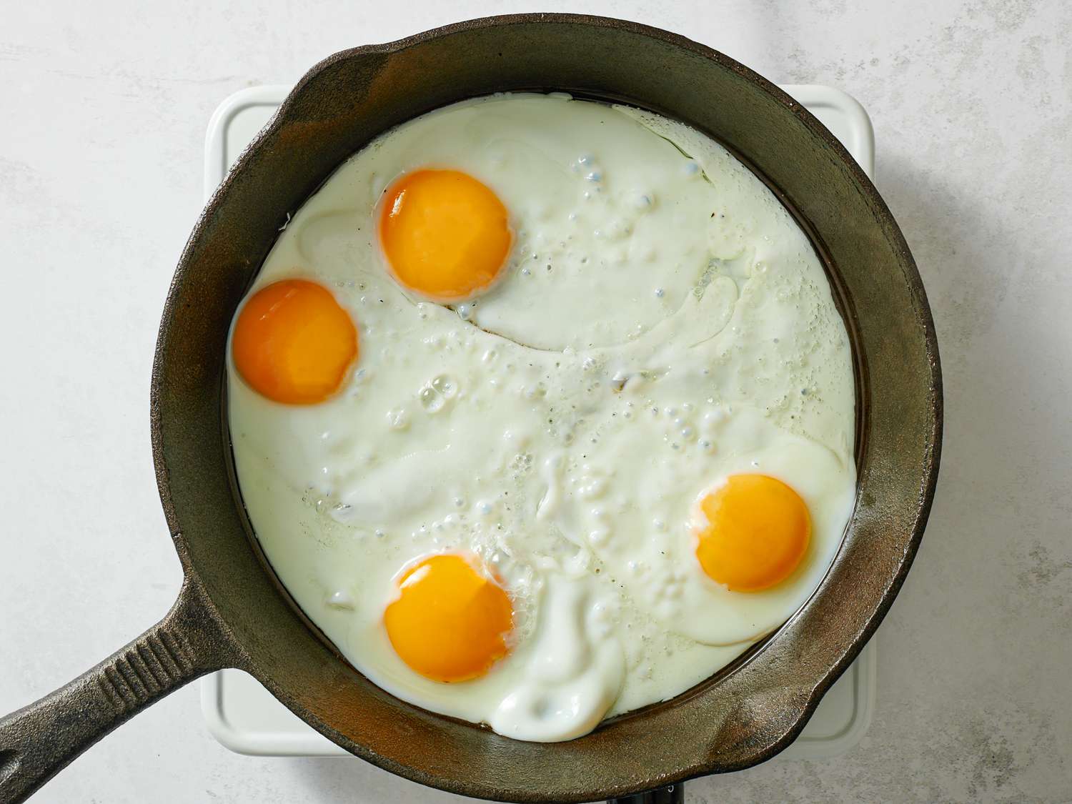 四个鸡蛋在铸铁煎锅里煮。蛋白凝固了，而蛋黄是完整的，仍然是流动的。