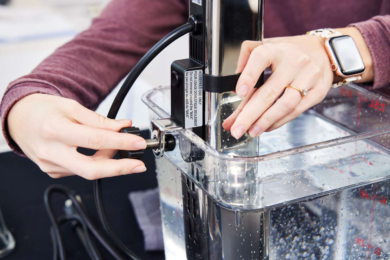 Two hands adjusting the clamp of a sous vide machine onto a Cambro container filled with water
