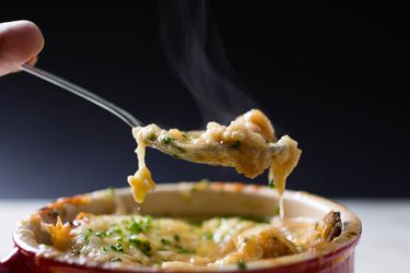 勺子取出一口cheese-topped法式洋葱汤从红色碗。