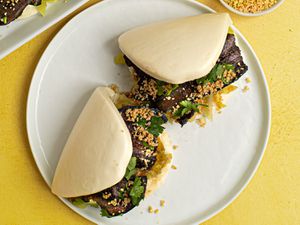 两个台湾五花肉包(瓜包)放在黄色背景的白色陶瓷盘子上。