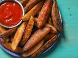 Closeup of a serving plate of roasted potato wedges with a ramekin of ketchup.