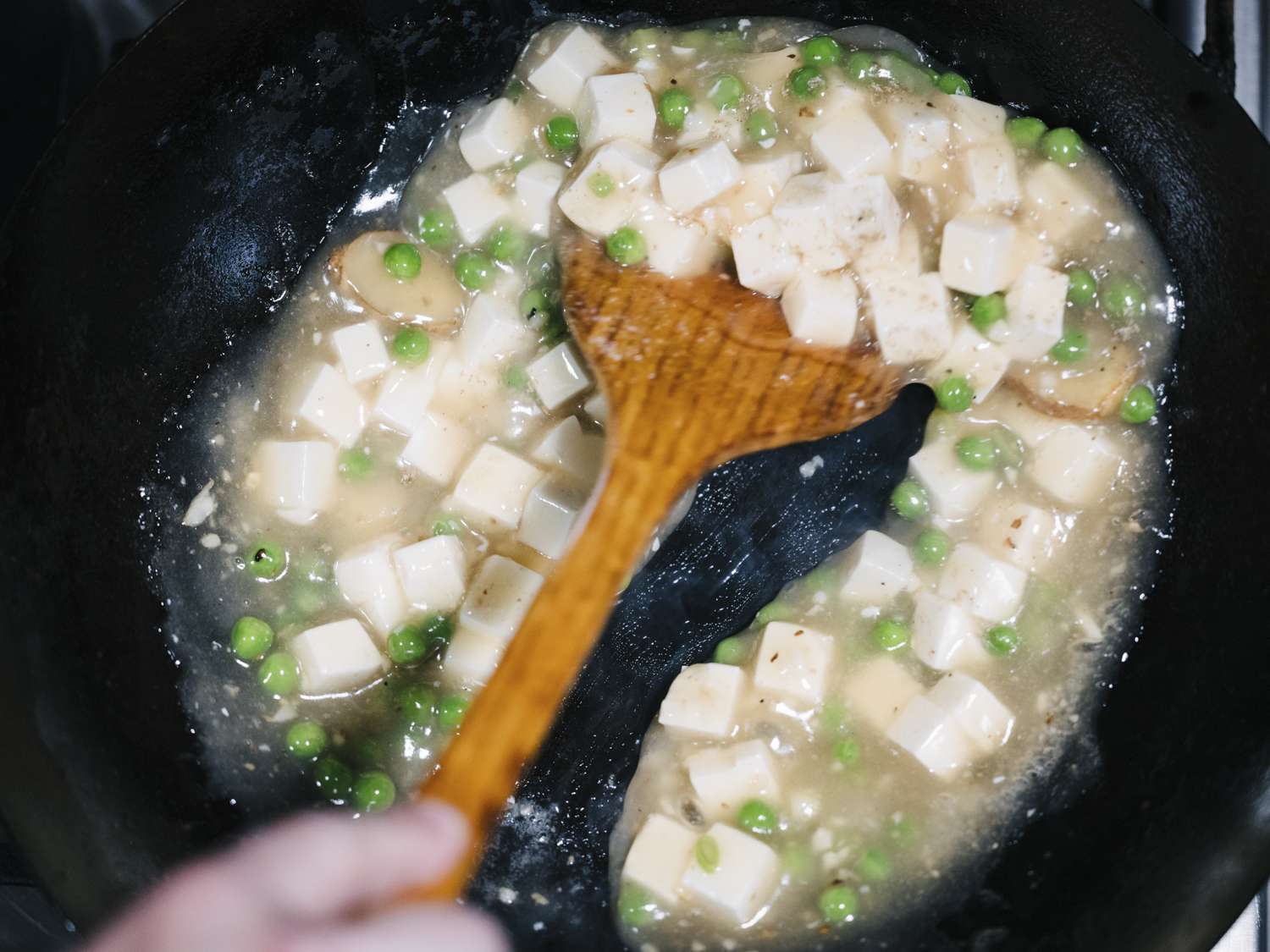 锅铲在锅里搅拌豌豆、豆腐和玉米淀粉浆，可以看出酱汁的粘稠度。