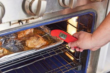 A person using a thermometer to take the temperature of chicken thighs roasting in the oven