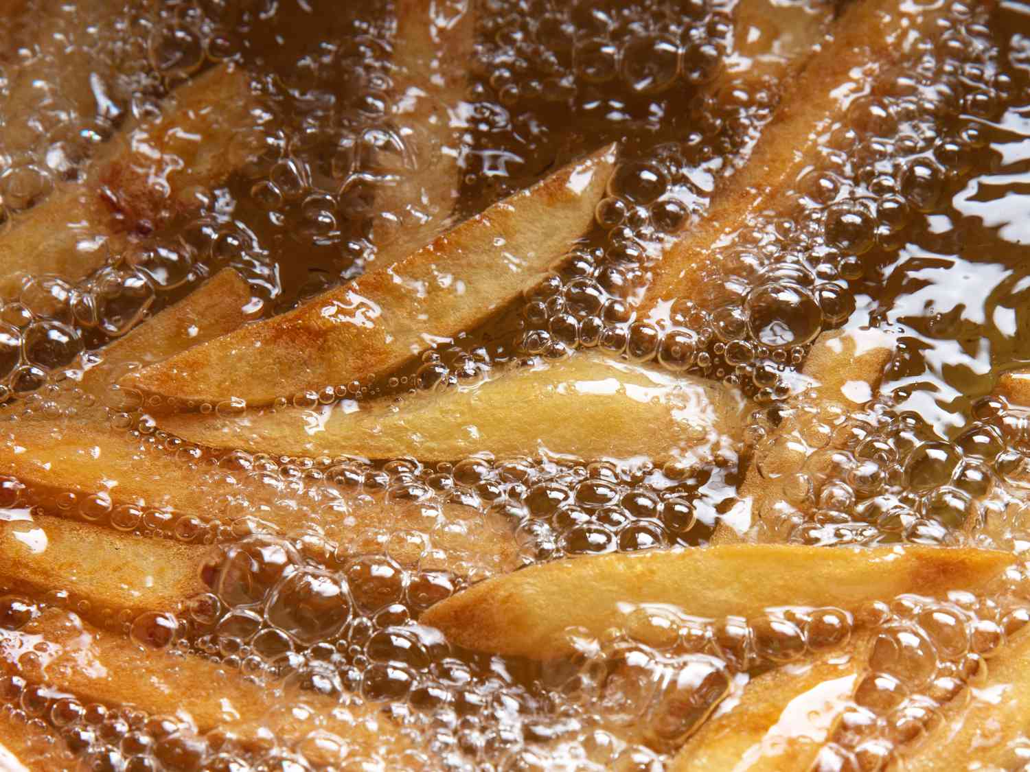 A close-up shot of thick-cut fries growing golden and crisp in hot oil.