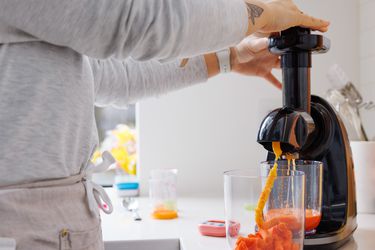 a person using a slow juicer to juice carrots