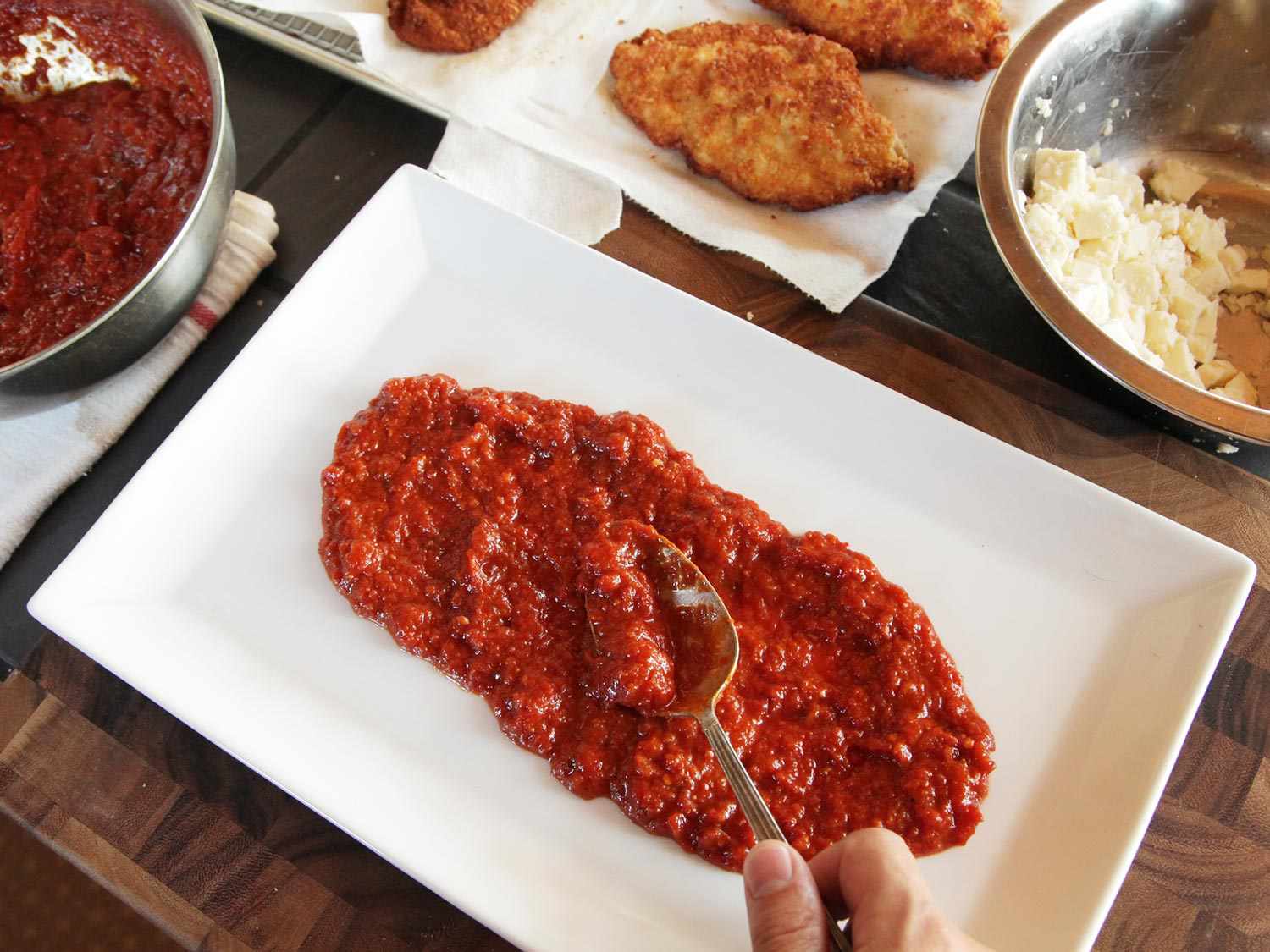 Laying down red sauce to build chicken parmesan