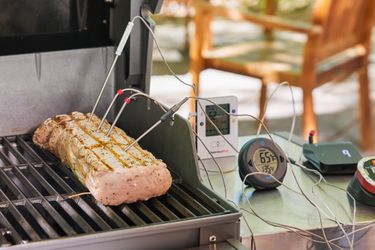 two thermometers on a grill table taking the temperature of a piece of meat cooking on the grill