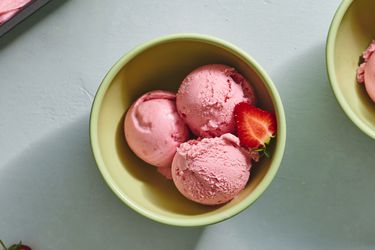 三勺草莓冰淇淋放在陶瓷碗里，还有半个新鲜草莓。
