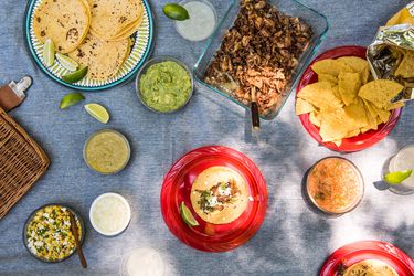 小吃、蘸料、玉米饼、青柠角、沙拉和蘸料作为墨西哥主题野餐的一部分，铺在野餐毯上。