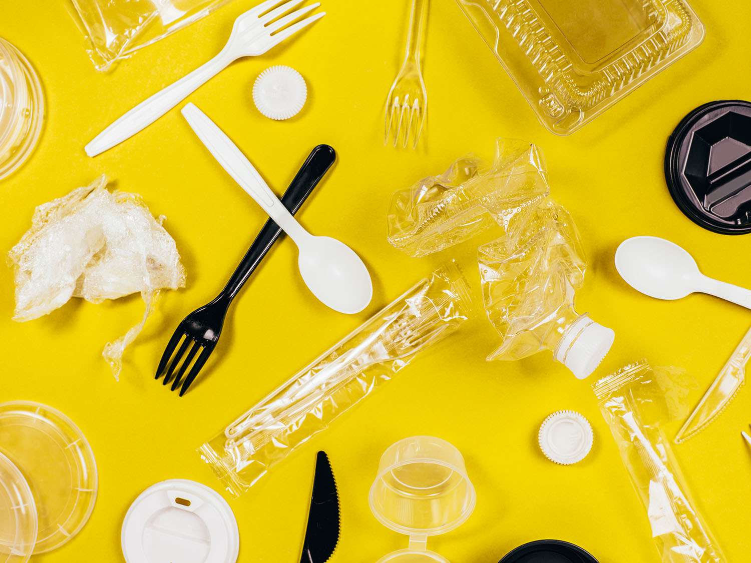 塑料勺子、叉子、食品容器、包装纸和黄色背景的瓶子