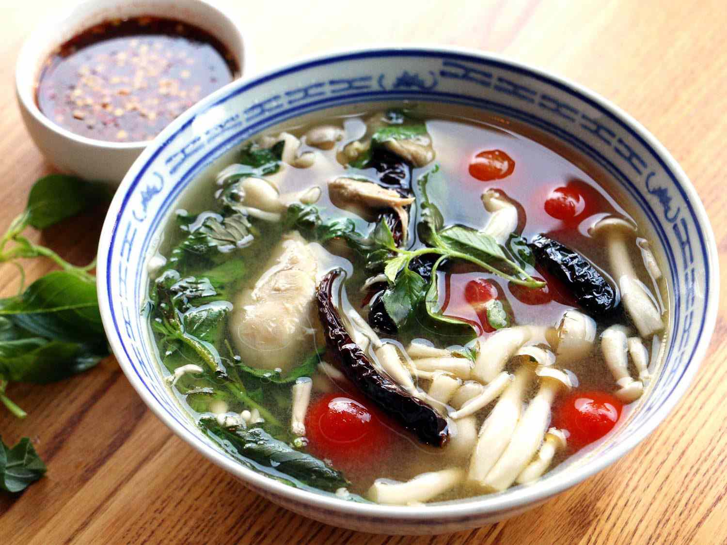 一碗蓝白相间的khao soi(宽米粉，西红柿，蘑菇和蔬菜在鸡汤里)，旁边是一小碗辣椒酱