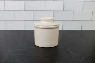 一个奶油色的陶瓷黄油钟形陶罐放在深色花岗岩台面上
