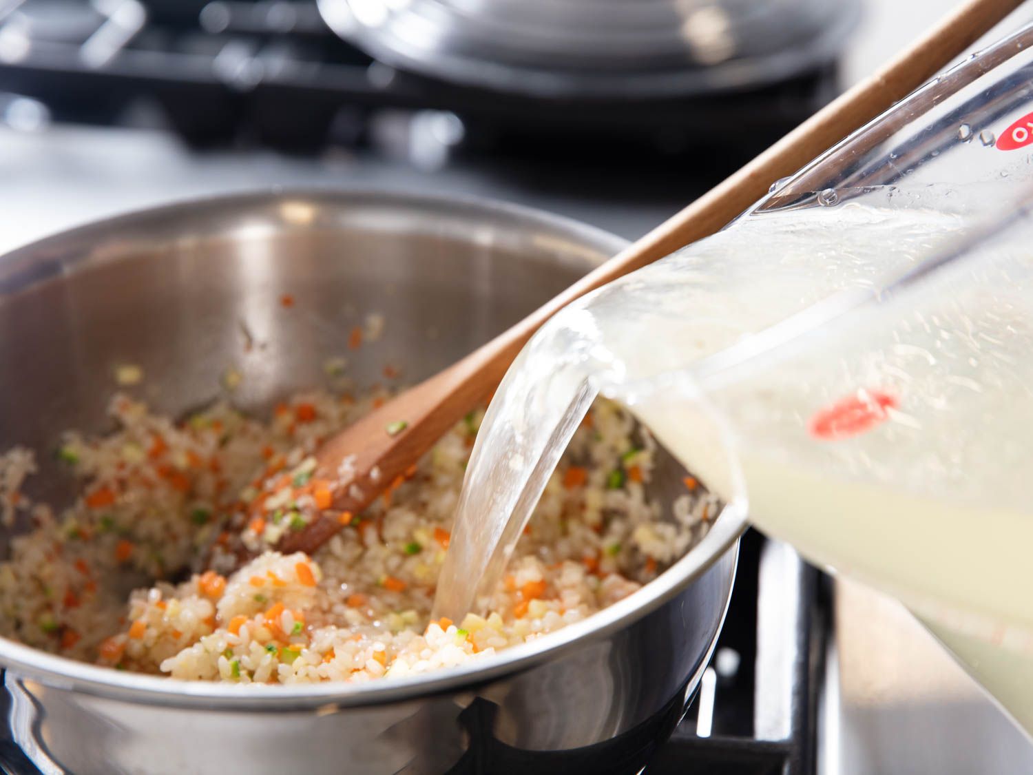 Pouring stock into a pot of rice and minced vegetables for juk