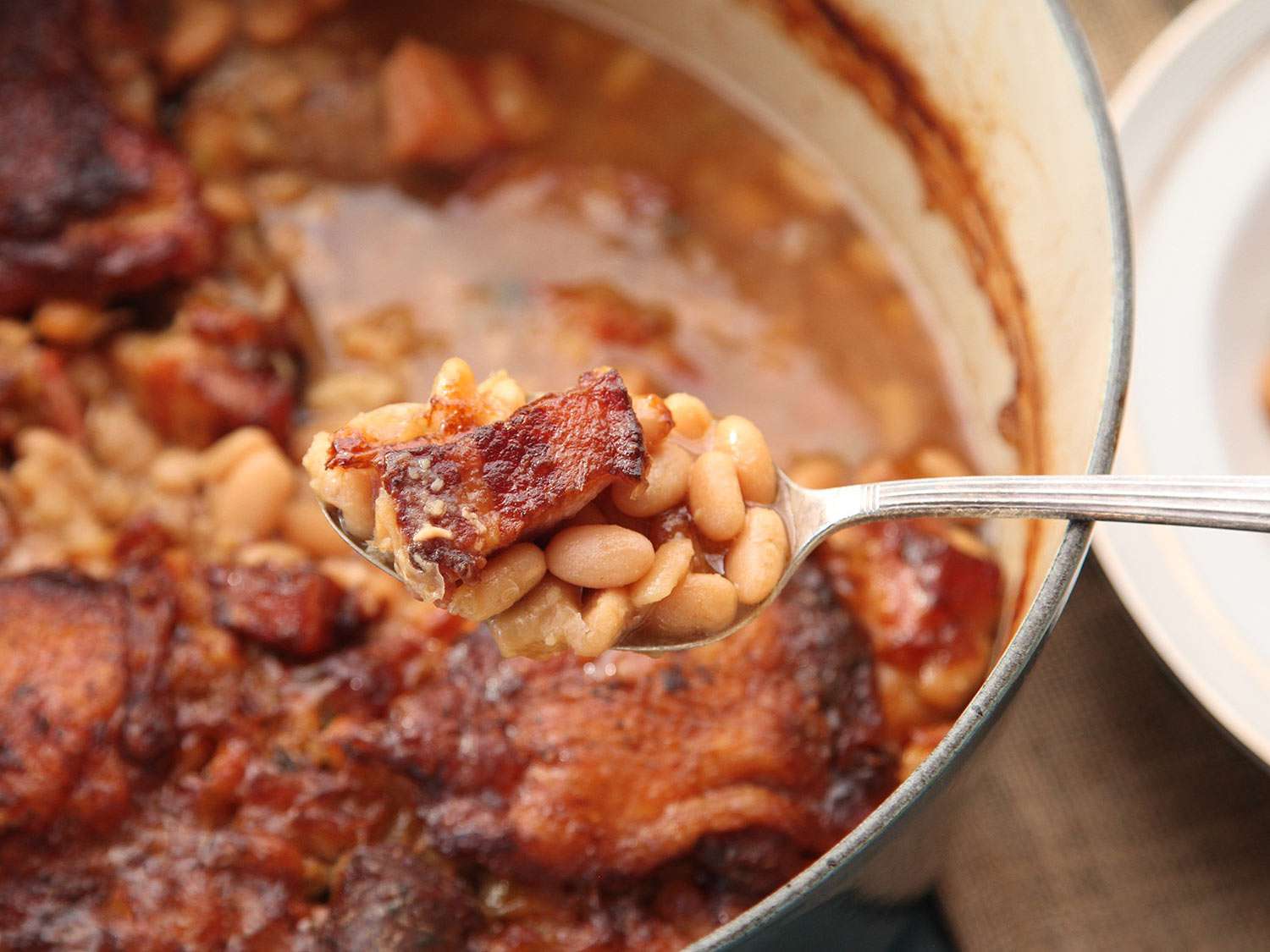 一勺嫩豆和褐色盐猪肉，从烤好的脆皮砂锅中取出。