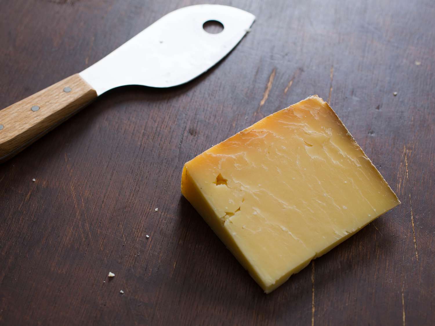 一块硬奶酪，旁边放一把奶酪刀。两人都在一张深色的木桌上。