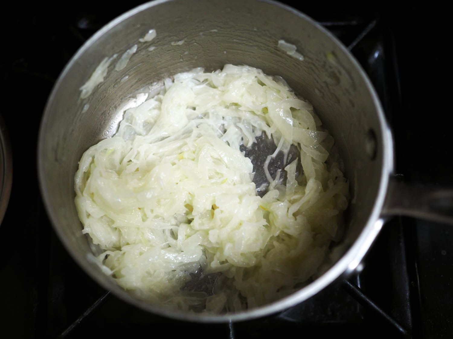 洋葱,脸色煞白,排干水,倒在平底锅里,展示了他们苍白的颜色。
