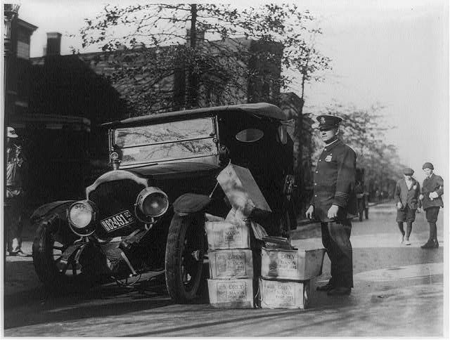 在一张黑白照片中，一辆破车和几箱私酿烈酒