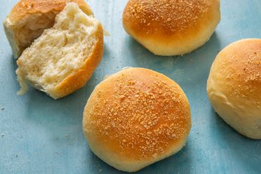 a few pandesal on a light blue background, one in the back split open to see inside