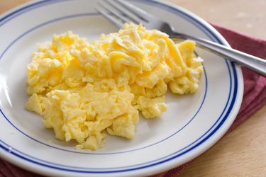 一个白蓝相间的盘子，上面有一堆蓬松的炒鸡蛋和一把叉子。