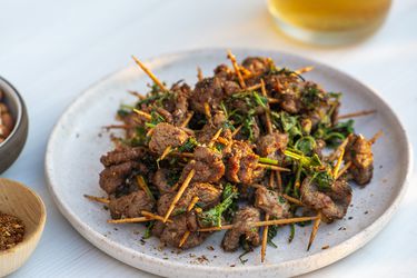 Plate of toothpick lamb set in front of out of focus glass of beer in background