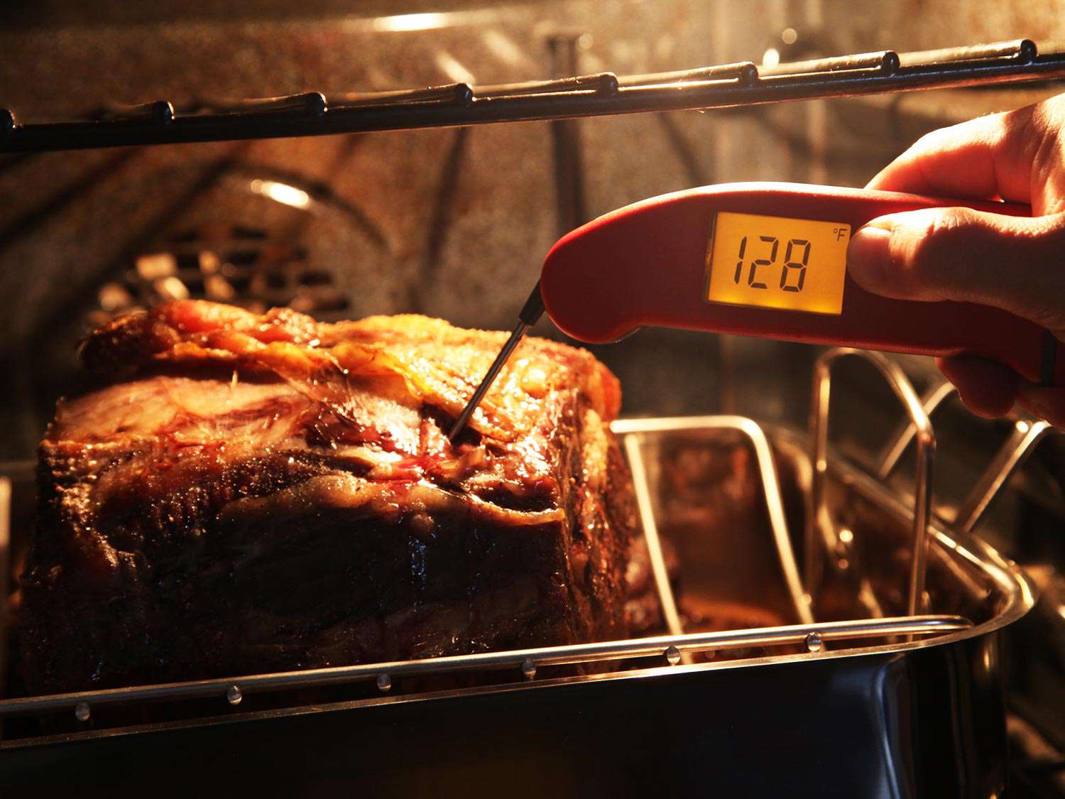 一只手将即时读数温度计插入烤架上烤好的肋排，读数为华氏128度。