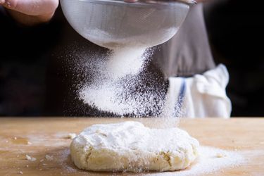 Sifting flour over the top of dough on a wood cutting board