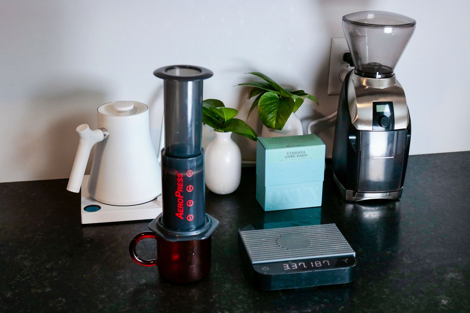 the aeropress on a black countertop with a coffee grinder and kettle in the background.
