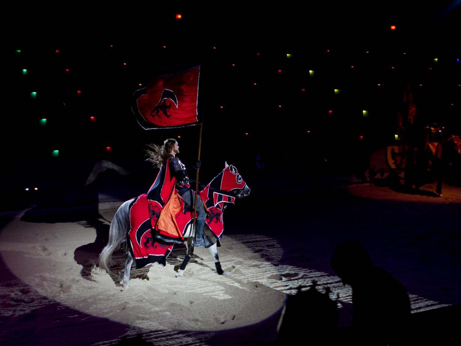 中世纪的红衣骑士，骑在马背上，穿着华丽的装饰，在竞技场的沙质地面上引人注目