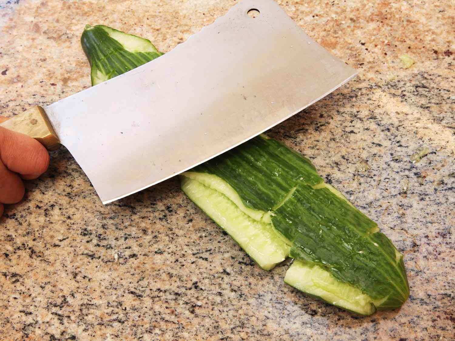 Smashing a cucumber on the counter with the flat side of a cleaver.