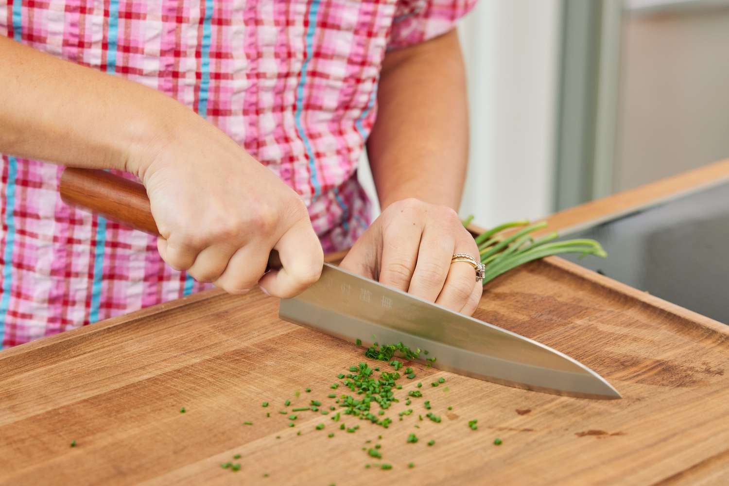 用厨师刀在木砧板上切韭菜的人