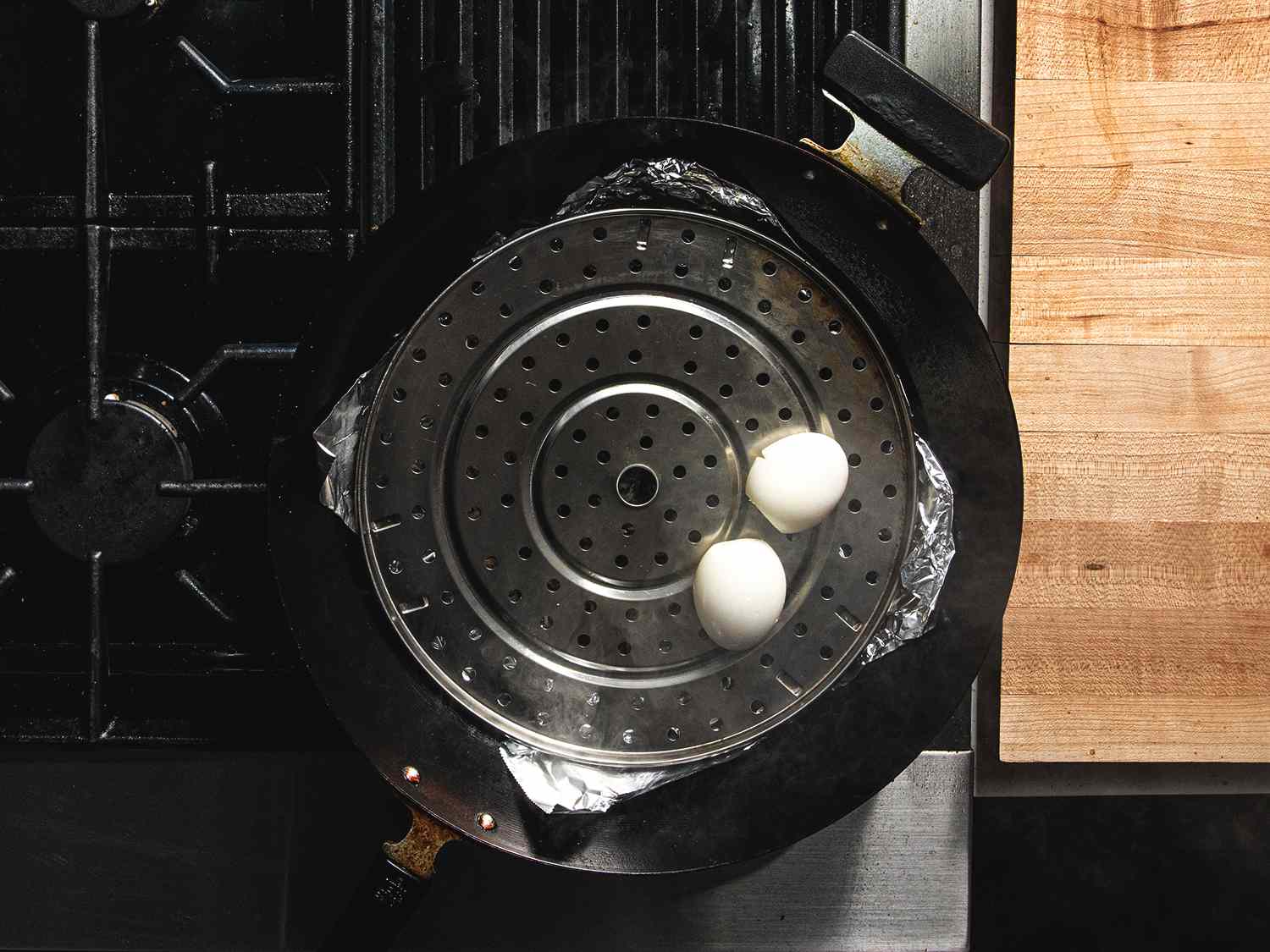 俯视图两个鸡蛋坐在穿孔架在锡箔内衬锅，准备熏制。