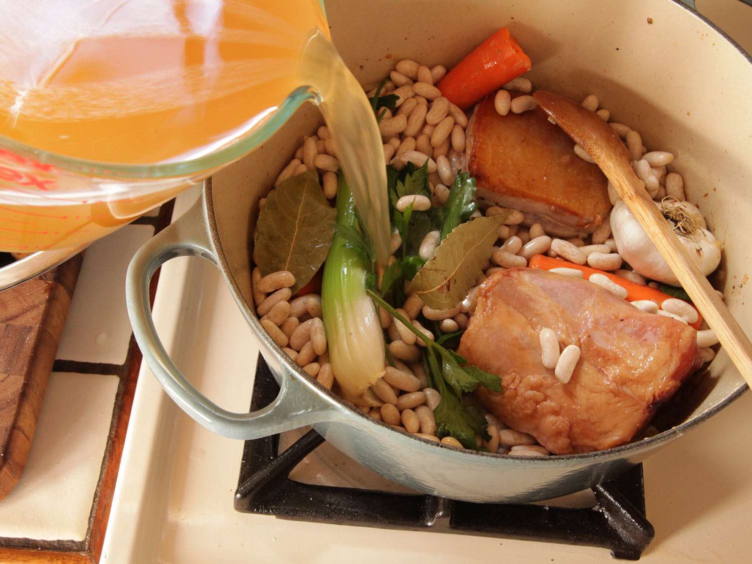 在干豆锅里加入高汤，腌猪肉，还有做豆焖肉的香料。