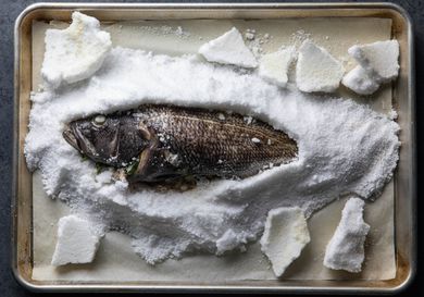 烤盘上的一整只烤黑鲈鱼被埋在一堆盐里，盐皮被敲碎并取出后，露出了水面。