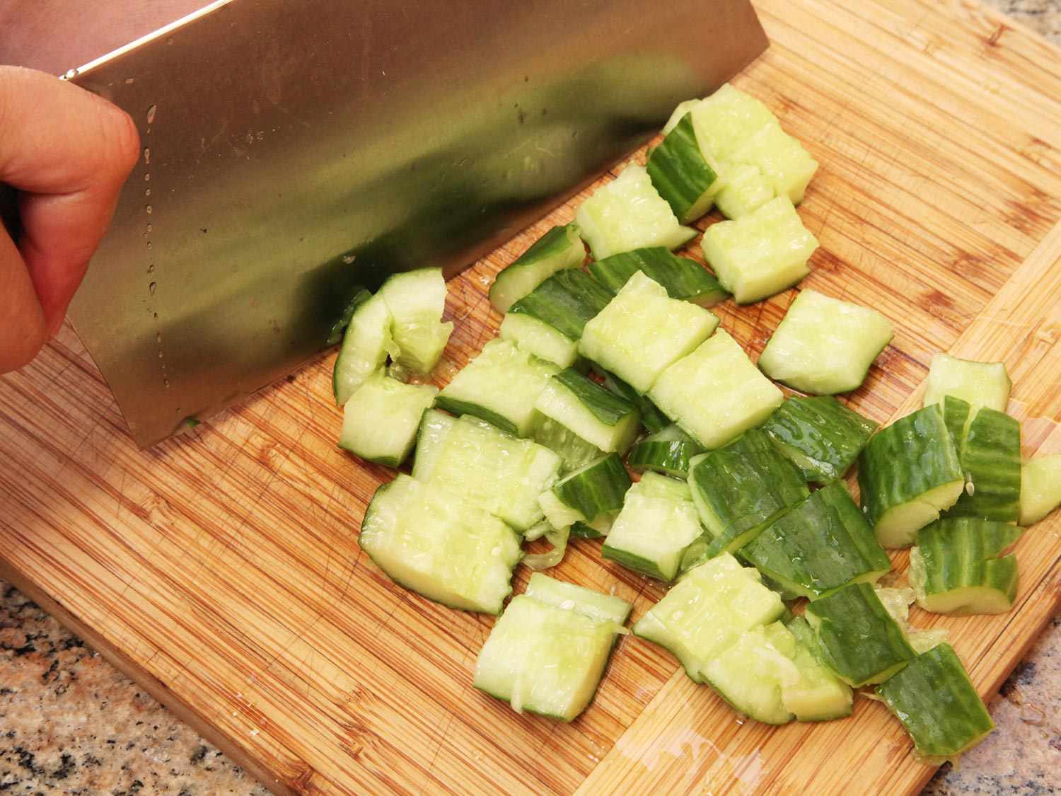 Using a cleaver to cross-cut smashed cucumbers.