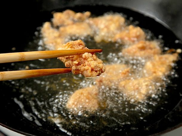 用筷子夹着一块炸鸡放在锅上，锅里放满热油和炸鸡。gydF4y2Ba