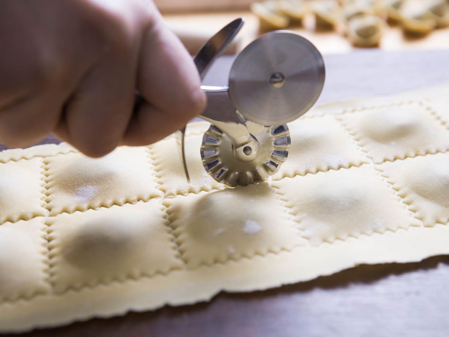 a hand using a pastry wheel to trim ravioli