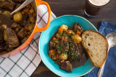 Pot of beef stew served at the table accompanied with a slice of bread and pint of stout