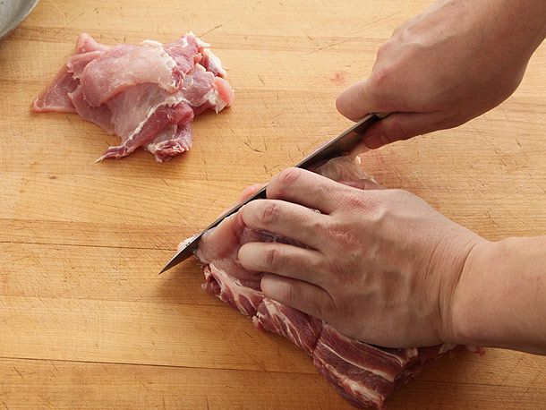 两只手用刀在木砧板上沿着纹理切西冷肉。