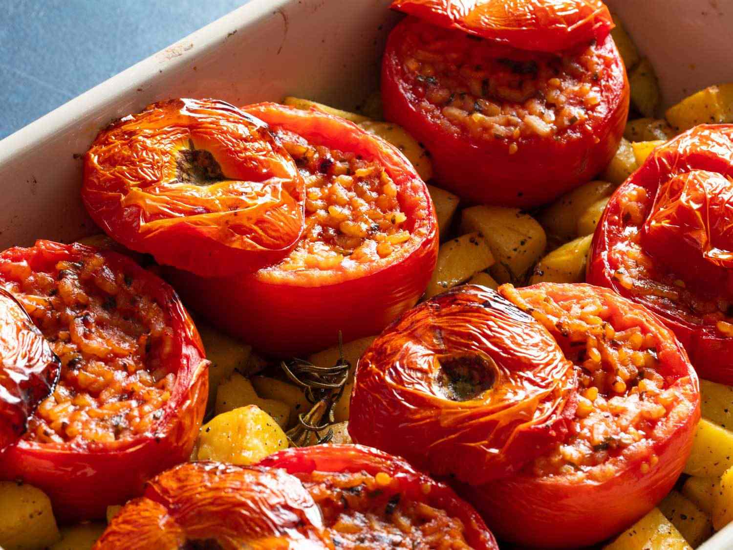 Close-up of rice-stuffed tomatoes in a baking dish with potatoes.